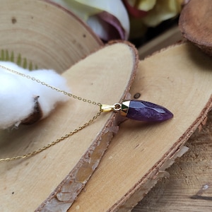 May include: A gold chain necklace with a purple amethyst pendant shaped like a point. The pendant is set in gold.