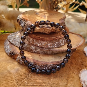 Può includere: Un braccialetto di pietre preziose marroni con perline sfaccettate. Il braccialetto è su una superficie di legno.