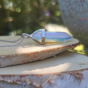 Op de afbeelding: Een zilveren ketting met een regenboogkleurige opaalpunt hanger. De hanger is gezet in een zilveren bezel en heeft een puntige vorm.