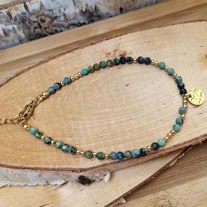 Könnte beinhalten: Ein türkisfarbenes und goldenes Perlen-Fußkettchen mit einem kleinen goldenen Anhänger. Das Fußkettchen besteht aus kleinen runden Perlen und einer zarten goldenen Kette.