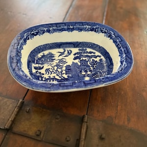 May include: Oval blue and white ceramic dish with a Willow pattern design. The dish features a detailed landscape scene with pagodas, trees, and a bridge. The rim has a decorative border. A classic piece for serving or display.
