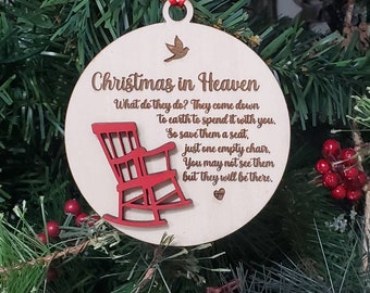 May include: A wooden Christmas ornament with the text "Christmas in Heaven" and a poem. The ornament features a red rocking chair cutout and a small bird. It hangs from a red ribbon, perfect for holiday decor.