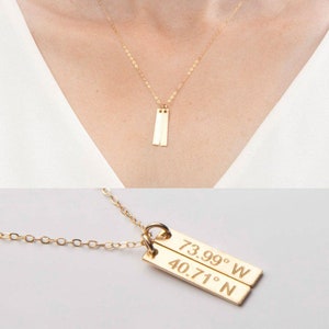 May include: Gold necklace with a double bar pendant engraved with the coordinates 40.71° N 73.99° W.