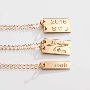 Peut inclure: Trois colliers en or avec des pendentifs en forme de barre personnalisés. Le pendentif du haut porte l'inscription "2016 S♥J", le pendentif du milieu porte l'inscription "Madeline Olivia" et le pendentif du bas porte l'inscription "Noah".