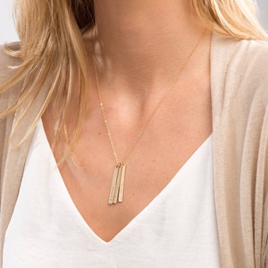Puede incluir: Un collar de oro con tres colgantes de barra vertical. Cada barra tiene una inscripción diferente.