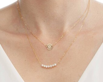 May include: A gold chain necklace with a small heart charm and a second chain with a row of pearls.