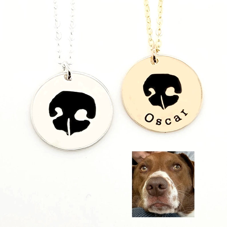 May include: Two silver and gold necklaces with a black dog nose print pendant. The gold necklace has the name "Oscar" engraved on the pendant.