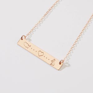 Puede incluir: Un collar de oro con un colgante de barra que presenta un contorno de los Estados Unidos, un corazón y un contorno de Irlanda. El colgante tiene tres puntos entre cada imagen.