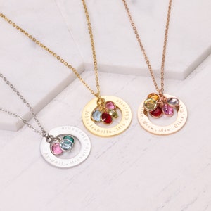 May include: Three gold necklaces with personalized engraved circles and colorful crystal charms. The necklaces are on a white marble background. The circles are engraved with names, including "John, Isabella, Mia, Charlotte", "Liam, Ava, Ella, Olivia", and "Abigail, Michelle, Sydney".