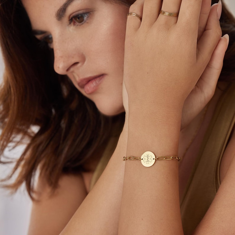 May include: Gold-toned medical alert bracelet. The bracelet features a chain link design with a circular pendant. The pendant displays the Star of Life symbol, a six-pointed star with a staff and snake.