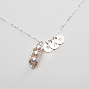 Puede incluir: Un collar de plata con un dije de vaina de guisante que contiene tres perlas blancas. El collar tambi&eacute;n tiene tres dijes de disco de plata con las letras 'E', 'A' e 'Y' grabadas en ellos.