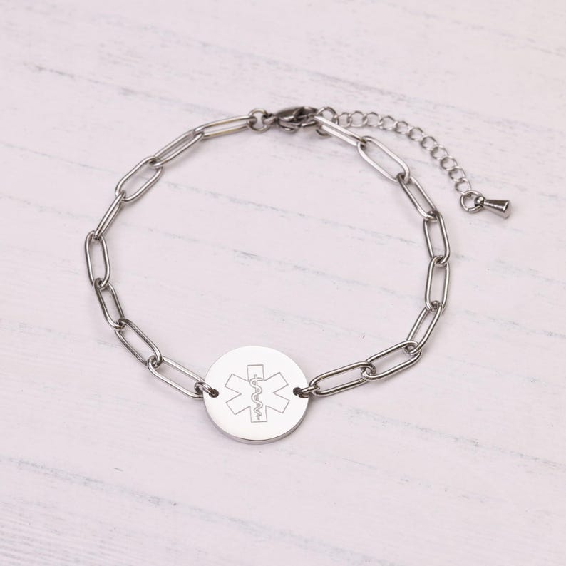 May include: A silver-colored medical alert bracelet with a chain link design. The bracelet features a circular pendant with the Star of Life symbol engraved on it. The bracelet is adjustable and has a lobster clasp closure.