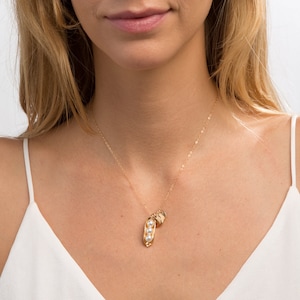 Puede incluir: Un collar de oro con un dije en forma de vaina de guisante y tres acentos de perlas. El dije est&aacute; unido a una delicada cadena de oro.