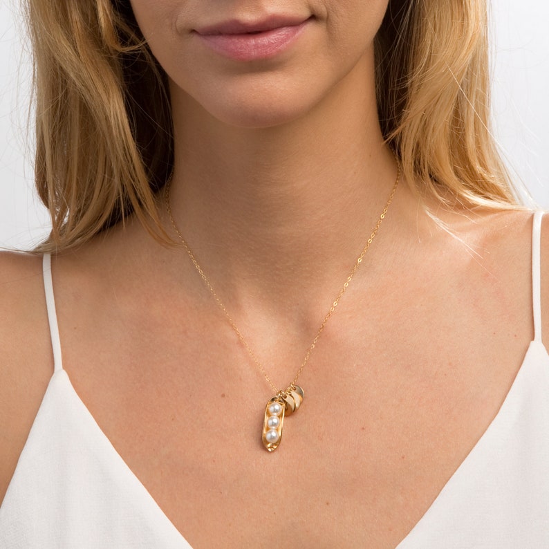 Puede incluir: Un collar de oro con un dije en forma de vaina de guisante y tres acentos de perlas. El dije est&aacute; unido a una delicada cadena de oro.
