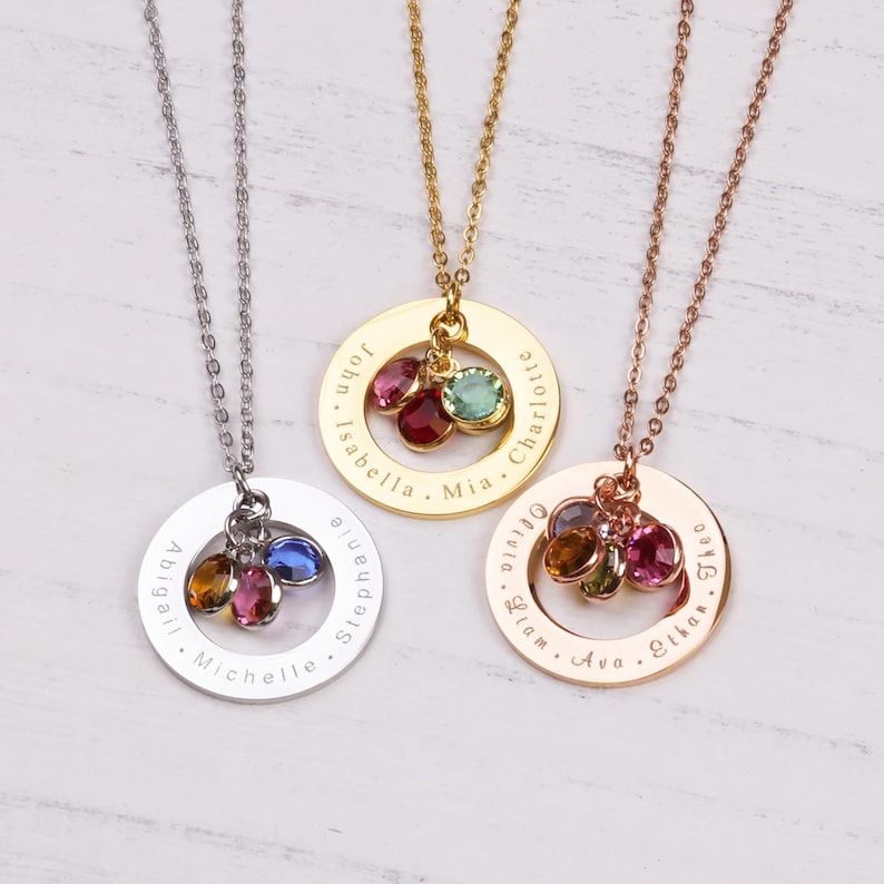 May include: Three gold, silver, and rose gold necklaces with personalized engraved circles and colorful gemstone charms. The circles are engraved with names, including John, Isabella, Mia, Charlotte, Abigail, Michelle, Stephanie, Olivia, Liam, Ava, Ethan, and Theo.