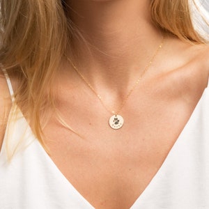 May include: Gold necklace with a round pendant featuring a paw print and the name "Rocky" engraved on it.