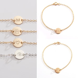 Op de afbeelding: Vier gouden kettingarmbanden met verschillende bedels. De bedels omvatten een ​​pootafdruk, een hart, de letter M en de letter B. Een armband heeft een zilveren ketting en een bedel met de letter B.