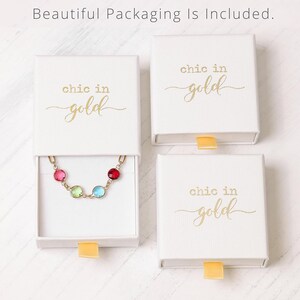 May include: White gift boxes with a gold inscription that reads "chic in gold". One box contains a gold chain with five colorful gemstones.