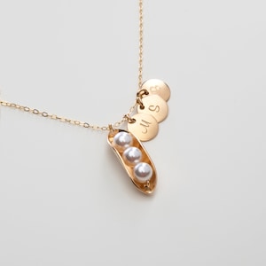 Puede incluir: Collar de oro con un dije en forma de vaina de guisante que contiene tres perlas y tres discos de oro grabados con las letras 'M', 'S' y 'B'.
