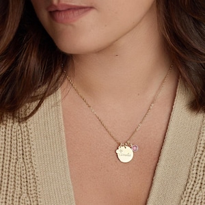 May include: A gold-toned necklace featuring a circular pendant engraved with the name Amelia and the number 16, accompanied by a small, round, pink-coloured gemstone charm. The pendant and charm hang from a delicate gold-toned chain.