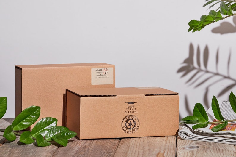 May include: Two brown cardboard boxes with printed text. The top box has the words "Start to Save Our Earth" and a green recycling symbol. The bottom box has the word "Glass" and a symbol of a glass dish.
