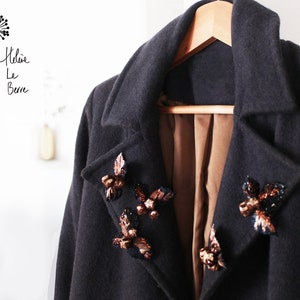 Peut inclure: Un manteau gris foncé avec une doublure marron et des embellissements décoratifs sur le col. Les embellissements sont faits de petites perles métalliques et ressemblent à des papillons.