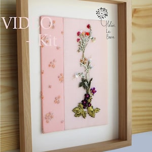 May include: Framed embroidery kit with a light pink background. The embroidery features a floral design with red, purple, and green. The frame is light-coloured wood. Text on the left says "VIDEO - Kit".