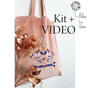 Op de afbeelding: Een roze fluwelen tote bag met een borduursel met bloemen. De tas heeft een witte achtergrond met kleurrijke bloemen en bladeren. De tekst "Kit + VIDEO" staat in zwart op de tas.
