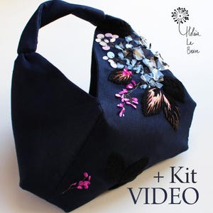 Peut inclure: Sac à main bleu marine avec un design structuré et une seule anse. Le sac est orné de broderies florales, de paillettes et d'éléments décoratifs en forme de cristaux dans des tons de rose, de bleu et de transparent. Le texte "+ Kit VIDEO" est visible.