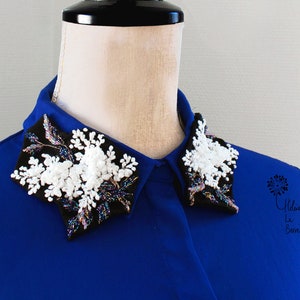 Op de afbeelding: Een koninklijk blauw overhemd met een zwarte en witte parelversiering op de kraag. De versiering heeft een bloemmotief met witte parels en iriserende pailletten.