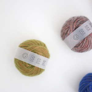 Puede incluir: Cuatro ovillos de lana en diferentes colores, cada uno con una etiqueta blanca que dice "GEEK". Los colores son verde, gris, azul y naranja.