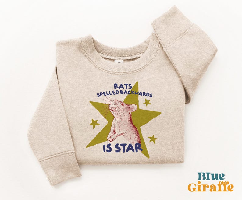 May include: A beige sweatshirt with a graphic of a rat inside a green star, with the text "RATS SPELLED BACKWARDS IS STAR". The sweatshirt has long sleeves and a crew neck.