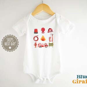 May include: White baby onesie with a watercolor design of fire safety equipment. The design includes a fire truck, fire hat, fire extinguisher, and other related items. The text "Blue Giraffe" is in the bottom right corner.
