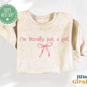 May include: A light pink sweatshirt with the text "i'm literally just a girl." in pink lettering and a pink bow.