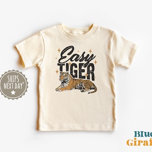 K&ouml;nnte beinhalten: Cremefarbenes Kinder-T-Shirt mit dem Schriftzug "Easy Tiger" in Schwarz und einer Illustration eines braun-schwarzen Tigers. Der Tiger liegt entspannt. Das T-Shirt hat kurze &Auml;rmel.