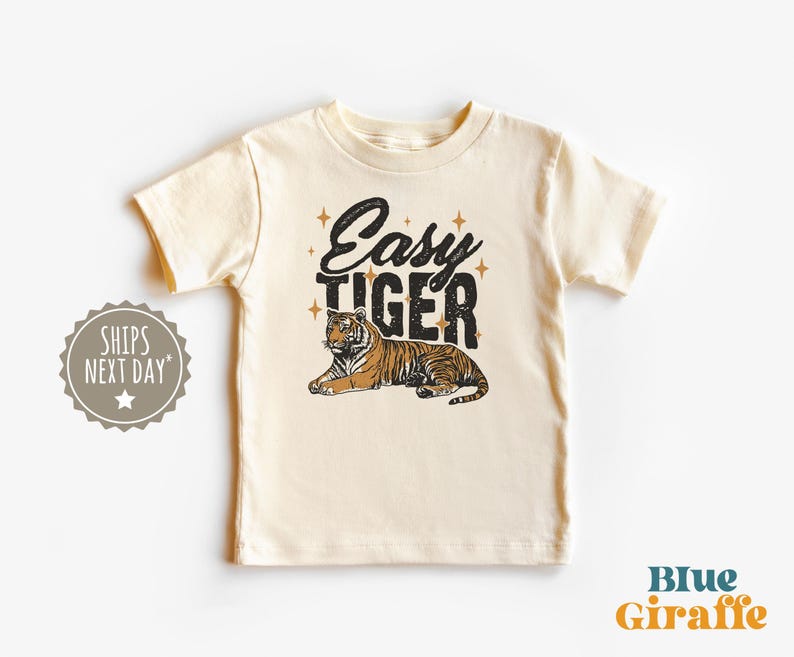 K&ouml;nnte beinhalten: Cremefarbenes Kinder-T-Shirt mit dem Schriftzug "Easy Tiger" in Schwarz und einer Illustration eines braun-schwarzen Tigers. Der Tiger liegt entspannt. Das T-Shirt hat kurze &Auml;rmel.