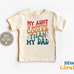 May include: A white t-shirt with the text "My Aunt is definitely cooler than my Dad" in colorful, retro-style lettering.