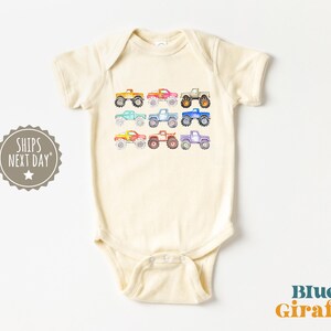 May include: A cream-colored baby onesie with a row of colorful monster trucks printed on the front. The trucks are in shades of red, orange, yellow, green, blue, purple, and pink.