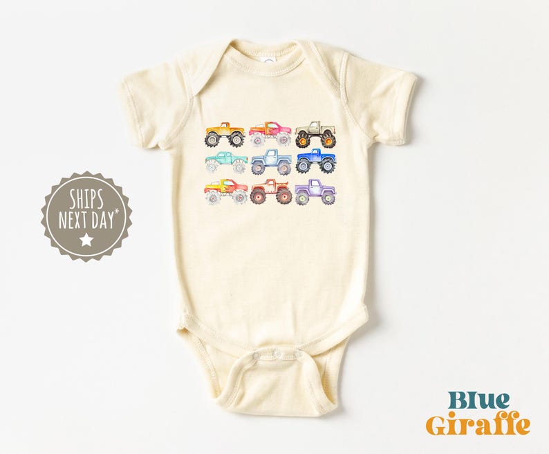 May include: A cream-colored baby onesie with a row of colorful monster trucks printed on the front. The trucks are in shades of red, orange, yellow, green, blue, purple, and pink.