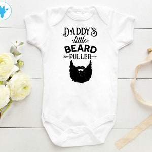 May include: White baby onesie with black text that reads "Daddy's little beard puller" with an arrow pointing to a black beard graphic.