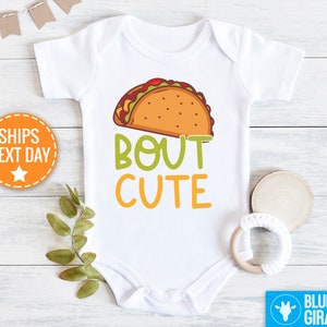 May include: White baby onesie with a cartoon taco and the text "Bout Cute".