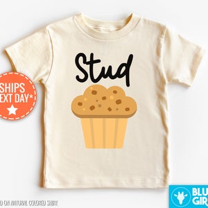 May include: A light beige t-shirt with the text "Stud" in black lettering and a cartoon muffin illustration.