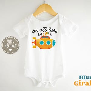 May include: White baby bodysuit with a yellow submarine graphic and the text "we all live in a".