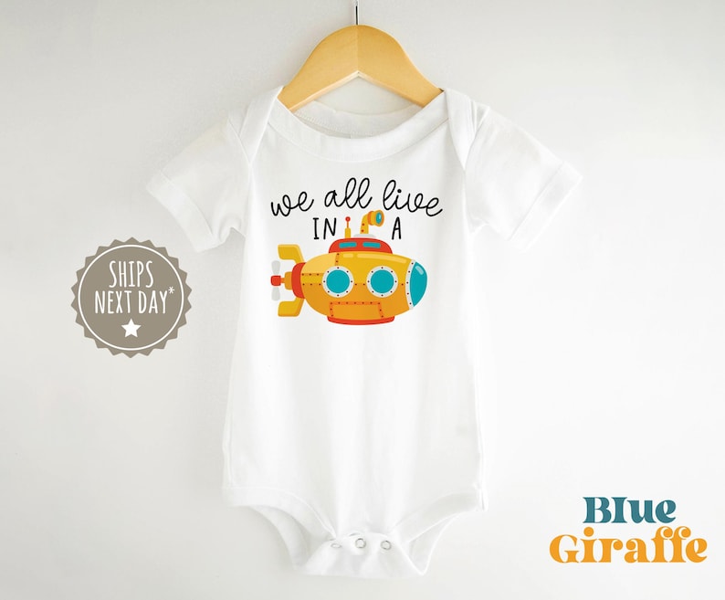 May include: White baby bodysuit with a yellow submarine graphic and the text "we all live in a".
