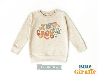 May include: A beige sweatshirt with the text "Two Groovy" in colorful retro lettering with peace signs and flowers.
