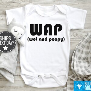 以下が含まれることがあります： 白いベビーロンパースに、黒い文字で「WAP（ウェットアンドプーピー）」と書かれています。
