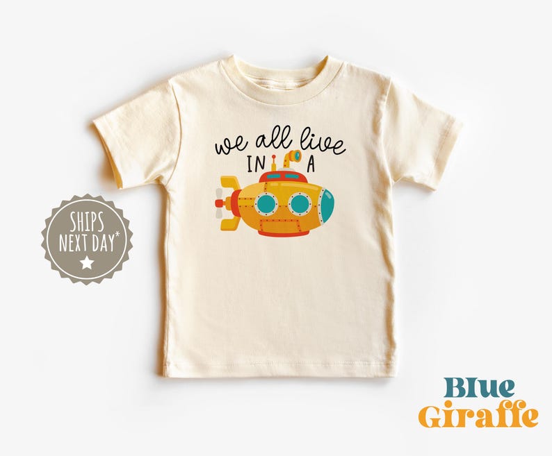 May include: A white t-shirt with a yellow submarine illustration and the text "we all live in a".