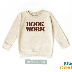 May include: A beige sweatshirt with the text "BOOK WORM" in brown letters.