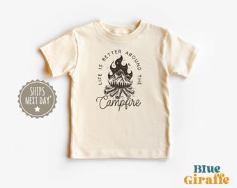 Op de afbeelding: Een crèmekleurig T-shirt met een zwart-witte afbeelding van een kampvuur met de tekst "Life is better around the campfire".