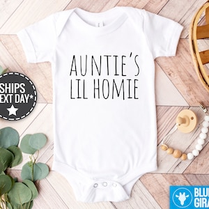 Peut inclure: Combinaison blanche pour bébé avec un texte noir qui dit "Auntie's Lil Homie".